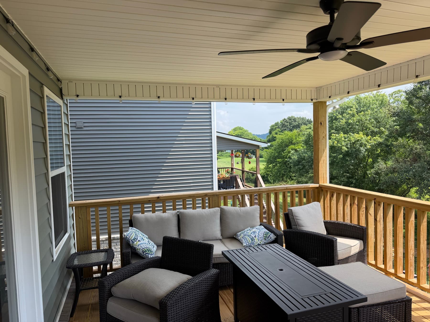 Furnished covered deck lounge with a ceiling fan and wood railing